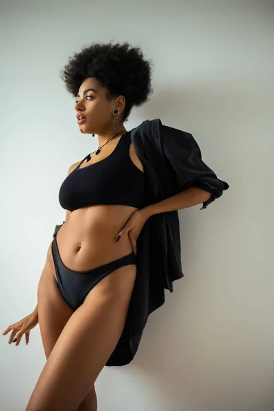 Pretty african american woman in shirt and underwear posing near white wall — Stock Photo
