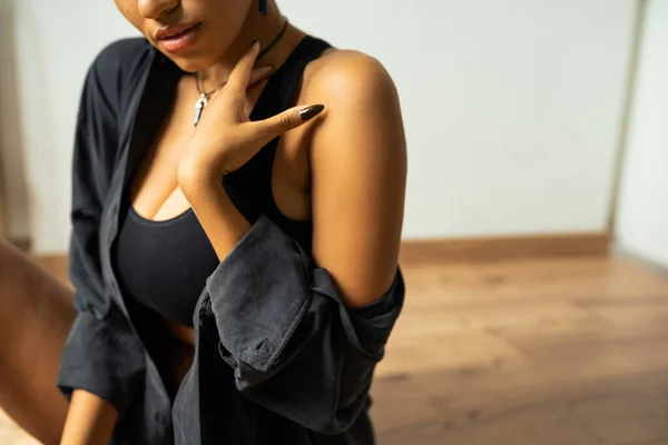 Vista ritagliata della donna afro-americana in crop top e camicia toccando il collo a casa — Foto stock