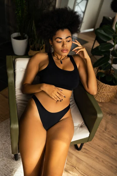 High angle view of sexy african american woman in crop top and panties sitting on armchair at home — Stock Photo