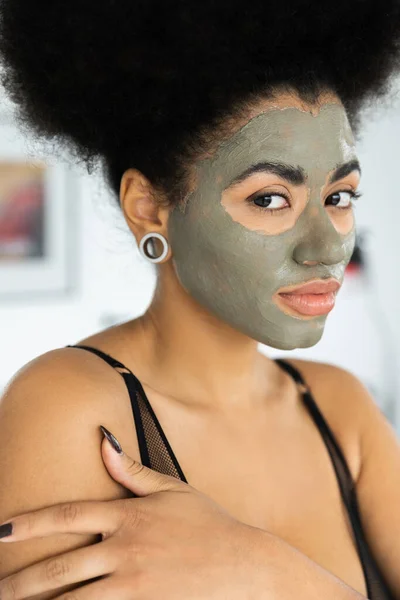 Portrait of african american woman with clay mask on face looking at camera at home — Stock Photo