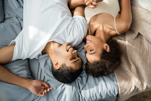 Vista dall'alto della felice coppia afro-americana che si tiene per mano e si guarda sul letto — Foto stock