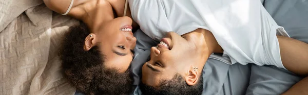 Vista superior de los amantes afroamericanos acostados en la cama y sonriendo el uno al otro, pancarta - foto de stock