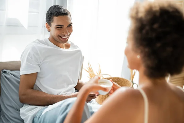 Trafitto africano americano uomo in bianco t-shirt sorridente a fidanzata offuscata in camera da letto — Foto stock