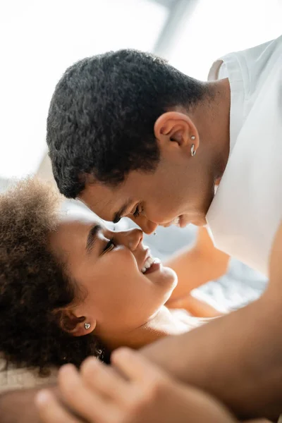 Vista lateral de pareja afroamericana sonriendo cara a cara en el dormitorio - foto de stock