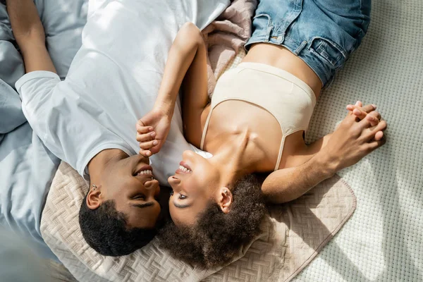 Top view of sexy african american woman touching chin of boyfriend while lying on bed — Stock Photo