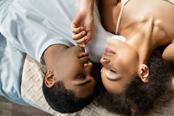 Top view of african american woman with closed eyes touching chin of young boyfriend on bed — Stock Photo