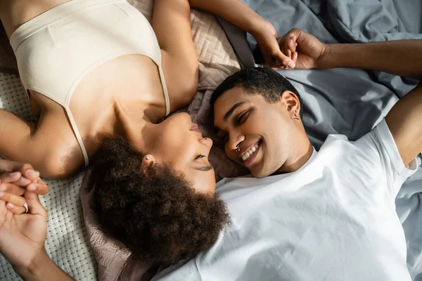 Вид сверху на счастливую африканскую пару, держащуюся за руки, лежащую на кровати с закрытыми глазами — стоковое фото