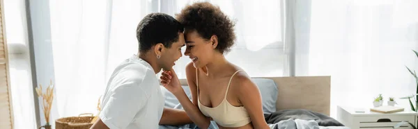 Happy african american woman smiling near boyfriend in white t-shirt in bedroom, banner — Stock Photo