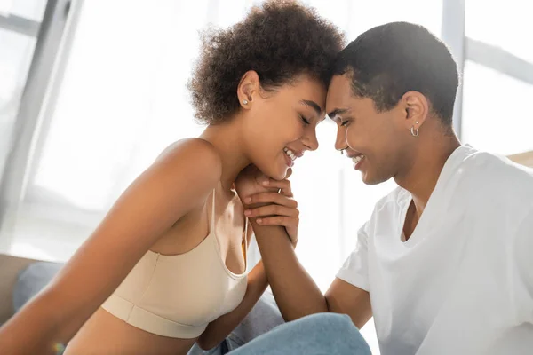 Vista laterale di africano americano uomo toccare il viso di bella e felice fidanzata a casa — Foto stock