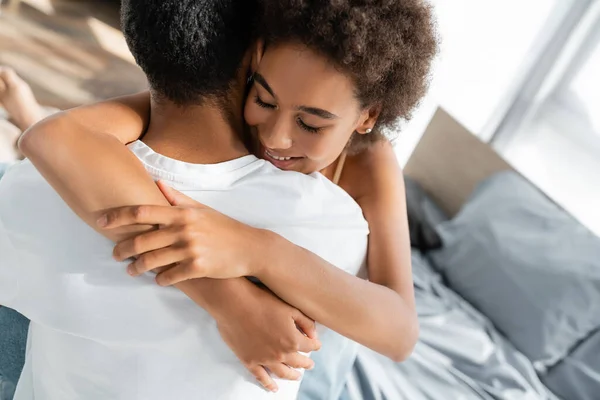 Mujer afroamericana feliz con los ojos cerrados abrazando novio en casa - foto de stock