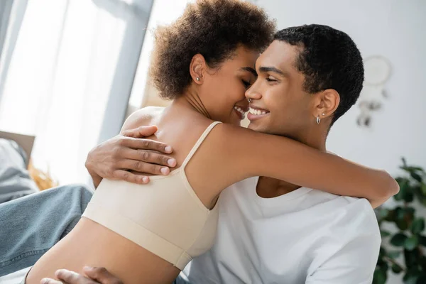 Glücklich afrikanisch-amerikanischer Mann mit piercing umarmt Freundin in Crop Top zu Hause — Stockfoto