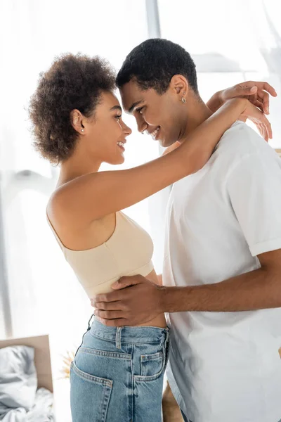 Vista lateral de la pareja afroamericana abrazando y sonriendo de pie cara a cara - foto de stock