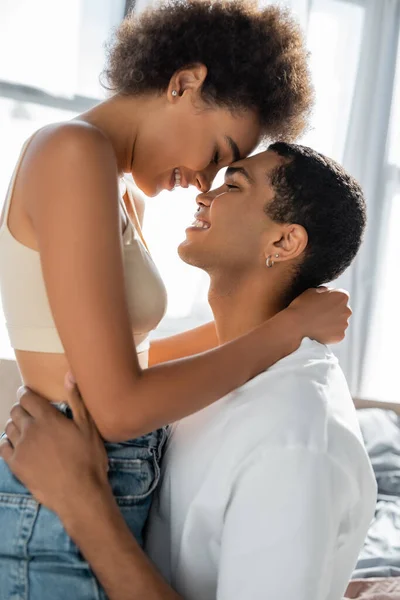 Vista lateral de pareja afroamericana abrazándose y sonriendo con los ojos cerrados - foto de stock