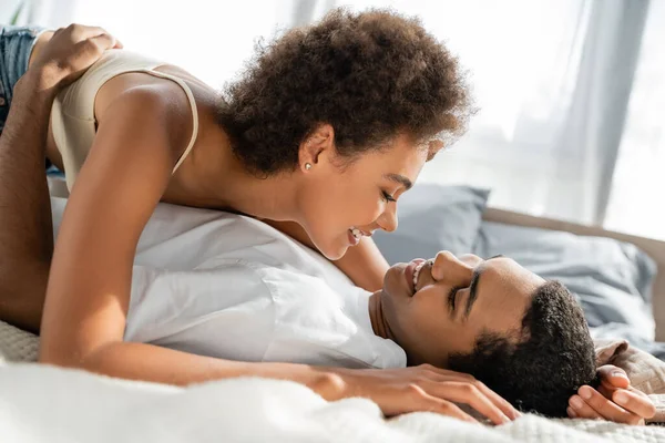 Кучерява афроамериканка посміхається біля хлопця лежить на ліжку вдома — Stock Photo