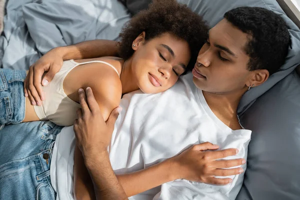 Vista superior de la pareja afroamericana con los ojos cerrados abrazando mientras está acostado en la cama - foto de stock