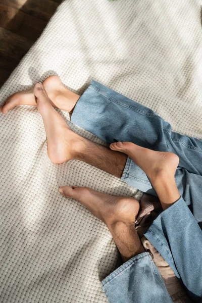 Top view of barefoot african american couple in jeans lying on bed at home — Stock Photo