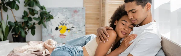 Young african american man embracing seductive woman smiling with closed eyes in bedroom, banner — Stock Photo