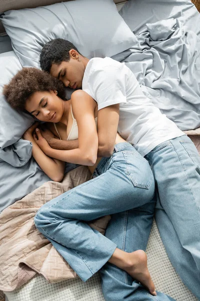 Vue de dessus du jeune couple afro-américain en jeans embrassant tout en dormant sur le lit à la maison — Photo de stock