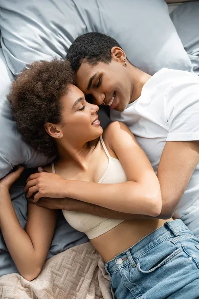 Vista superior do casal americano africano satisfeito abraçando enquanto deitado na cama — Fotografia de Stock