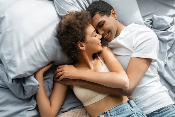 Vista superior da mulher americana africana no topo da colheita e homem em t-shirt abraçando com os olhos fechados na cama — Fotografia de Stock