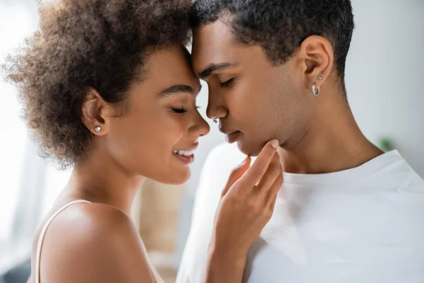 Side view of smiling and tender african american woman touching chin of young boyfriend — Stock Photo