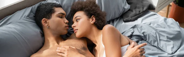 High angle view of sexy african american couple looking at each other on bed, banner — Stock Photo