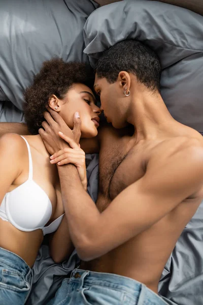 Vista superior do homem americano africano sem camisa beijando mulher sexy no sutiã branco na cama — Fotografia de Stock