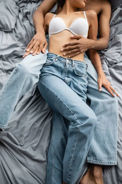 Cropped view of young and sexy african american lovers lying in jeans on grey bedding — Stock Photo