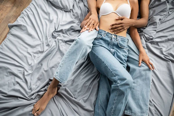 Вид зверху обрізаної афроамериканської жінки в джинсах і білий бюстгальтер лежить біля молодого хлопця — стокове фото