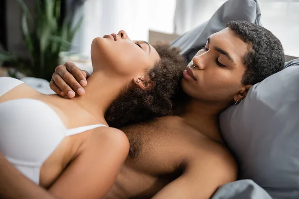 Sexy africano americano hombre con piercing abrazando apasionada novia en la cama - foto de stock