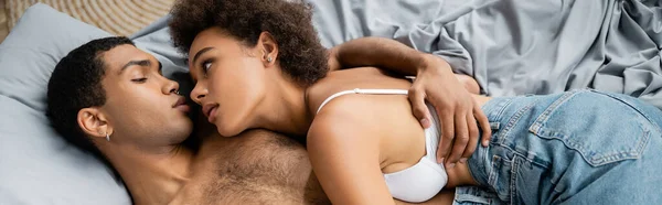 Top view of young african american lovers hugging on bed at home, banner — Stock Photo