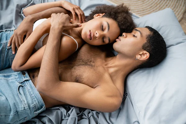 Vue grand angle de sexy jeune homme afro-américain embrassant petite amie couché avec les yeux fermés — Photo de stock