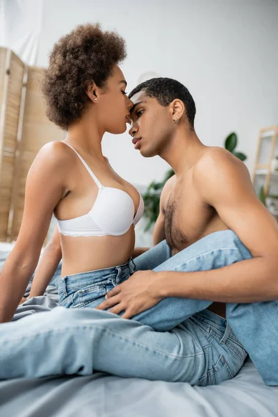 Vista laterale di uomo e donna afroamericano senza maglietta in reggiseno bianco sul letto a casa — Foto stock
