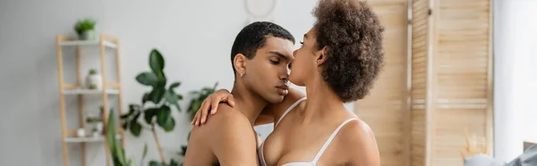 Африканский мужчина без рубашки обнимает девушку с сексуальной грудью дома, баннер — стоковое фото
