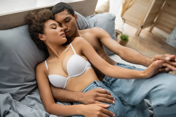 Blick aus der Vogelperspektive auf ein verführerisches afrikanisch-amerikanisches Paar, das sich im Bett an den Händen hält — Stockfoto