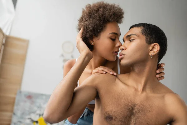 Morena rizada mujer abrazando sin camisa perforado africano americano novio en casa - foto de stock