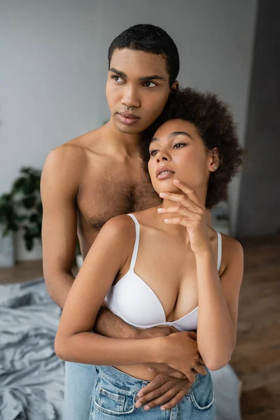 Femme afro-américaine passionnée en soutien-gorge blanc regardant loin près de copain torse nu — Photo de stock