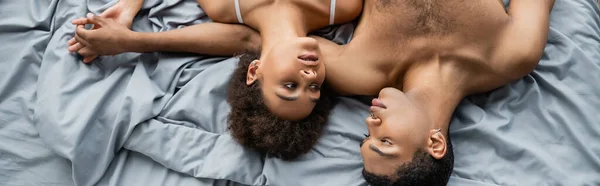 Vista superior dos amantes afro-americanos olhando uns para os outros e de mãos dadas na cama, bandeira — Fotografia de Stock