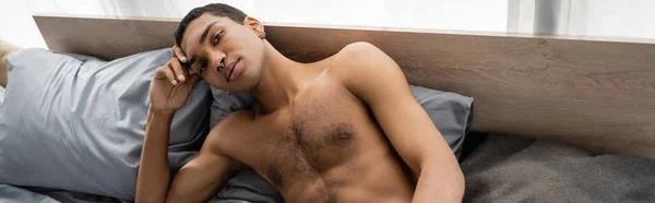 Sexy african american man with shirtless muscular torso looking at camera on bed at home, banner — Stock Photo