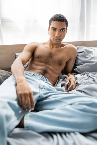Sexy and muscular african american man in jeans looking at camera on grey bedding, banner — стоковое фото