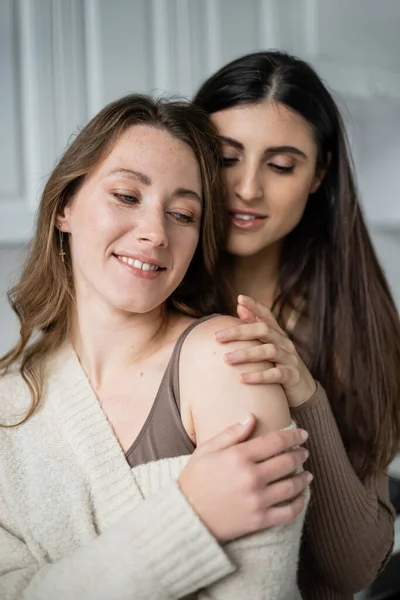 Усміхнена лесбіянка обіймає партнера в теплому светрі вдома — стокове фото