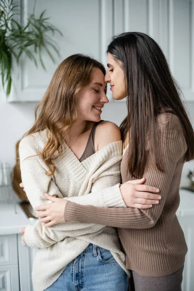 Молодая лесбиянка обнимает партнера в свитере на кухне — стоковое фото