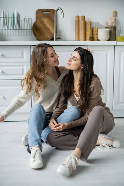 Young lesbian woman touching brunette girlfriend on floor in kitchen — Stock Photo