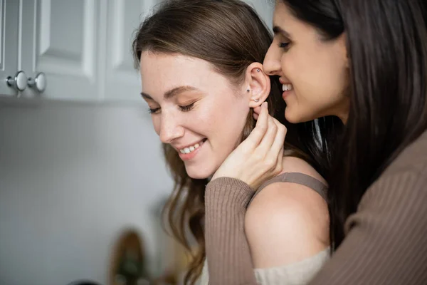 Позитивная женщина трогает ухо подруги на кухне дома — стоковое фото