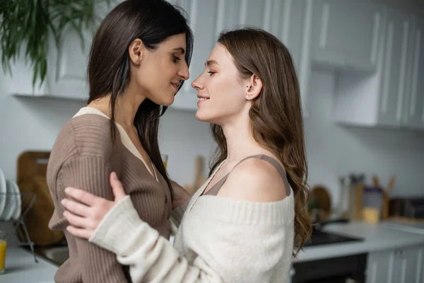 Seitenansicht eines lesbischen Paares, das sich in der Küche umarmt und anschaut — Stockfoto