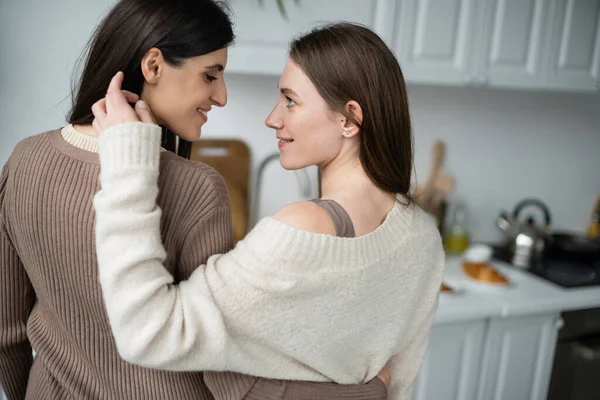 Vista laterale della donna lesbica sorridente che tocca i capelli del partner in cucina — Foto stock