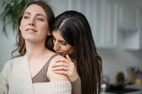Молодая женщина целует плечо лесбиянки партнера на кухне — стоковое фото