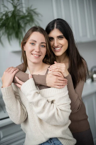 Позитивна одностатева пара в теплому одязі обіймається на кухні — стокове фото