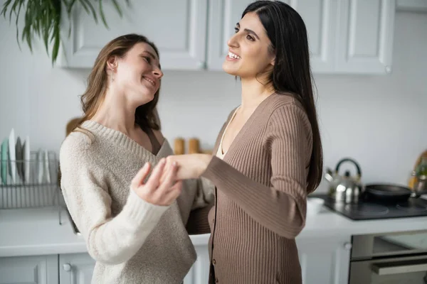 Cheerful same sex couple in warm clothes holding hands in kitchen — Stock Photo