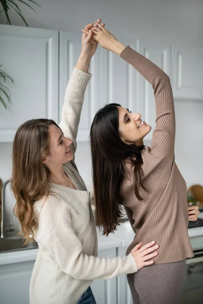 Улыбающиеся лесбиянки держатся за руки, танцуя на кухне — стоковое фото